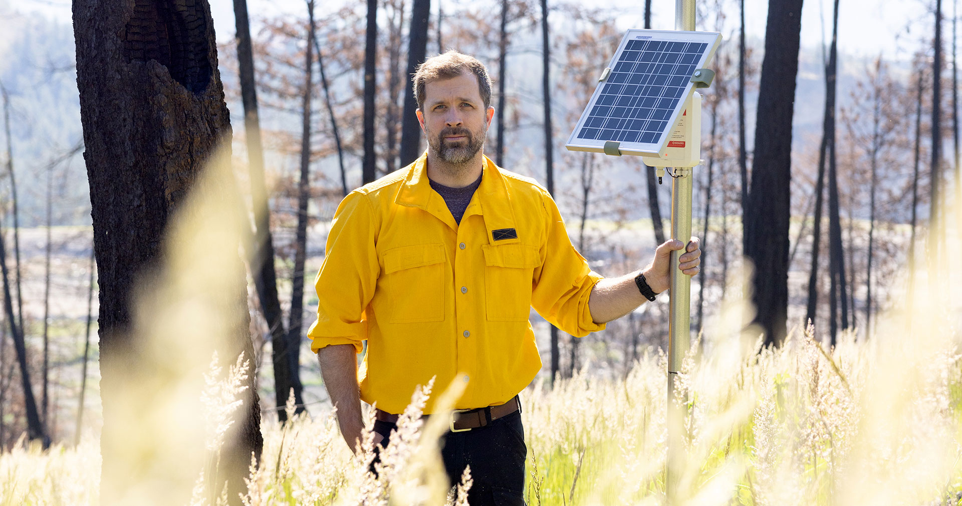 Dr. Mathieu Bourbonnais standing amid trees and vegetation holding a Wildfire sensor