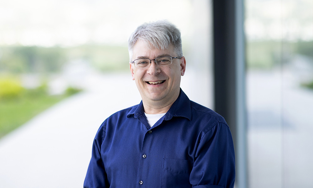 Male professor smiles while leaning against a wall